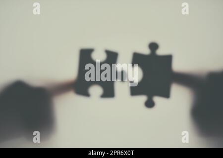 Could this be that perfect fit. Defocussed shot of two unrecognizable businesspeople holding two puzzle pieces together. Stock Photo