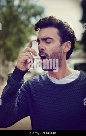 Getting his symptoms under control. Cropped shot of a young man using his asthma pump outside. Stock Photo