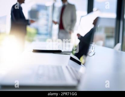 Business in focus. Shot of an open laptop on a boardroom desk with two businessmen blurred in the background. Stock Photo