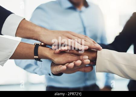 Lets bring it in. Closeup of a group of unrecognizable businesspeople forming a huddle with their hands inside of the office during the day. Stock Photo