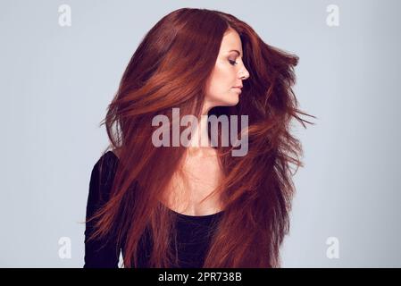 Lovely luscious locks. Studio shot of a young woman with beautiful red hair posing against a gray background. Stock Photo