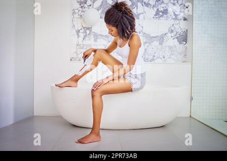 Dress season is here again. Shot of an attractive young woman shaving her legs with a razor and shaving cream in the bathroom. Stock Photo
