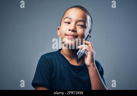 So youre telling me this is the tooth fairy.... Studio shot of a cute little boy using a smartphone against a grey background. Stock Photo
