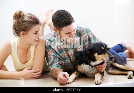 Hes a couples best friend. Shot of an affectionate young couple lying on the floor with their dog. Stock Photo
