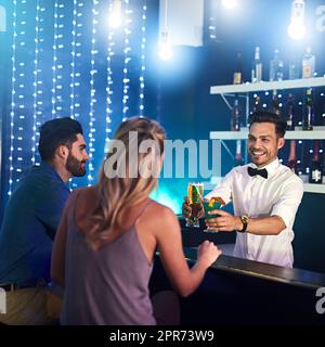 His skill and personality keep his customers satisfied. Shot of a happy bartender serving drinks to a couple in a nightclub. Stock Photo