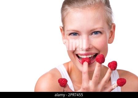 Berry delicious. Shot of a beautiful young woman playfully eating raspberries off her fingertips. Stock Photo