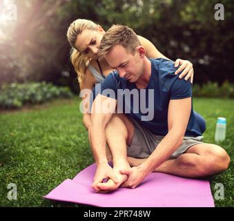 I might have pinched a nerve. Shot of a young man suffering from a foot injury while working out with his girlfriend outdoors. Stock Photo