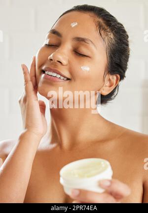 You glow differently when youre actually happy. Shot of young woman using with facial moisturiser at home. Stock Photo