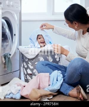 Can you see me mom. Shot of a young mother playfully bonding with her baby girl while doing the laundry at home. Stock Photo