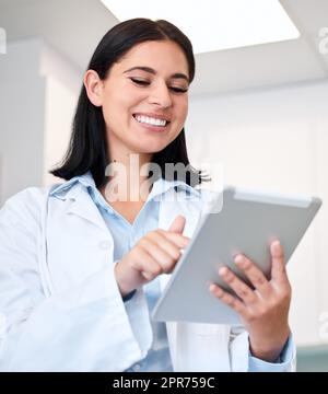 A confident, young female dentist working on her digital tablet in the doctors room. A beautiful and professional young woman working in a dental office. Oral health resources are easy to find online Stock Photo
