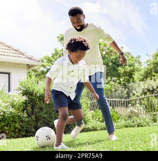 They have so much energy today. Shot of a father and son playing soccer together outdoors. Stock Photo