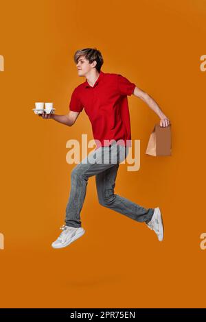 Delivery man in red cap, t-shirt holding cardboard box, coffee and jumping Stock Photo