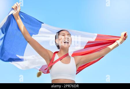 French athlete celebrating her gold medal olympic win, flying a flag. Smiling fit active sporty woman feeling motivated. Celebrating national pride and achieving gold medal in olympic sport Stock Photo