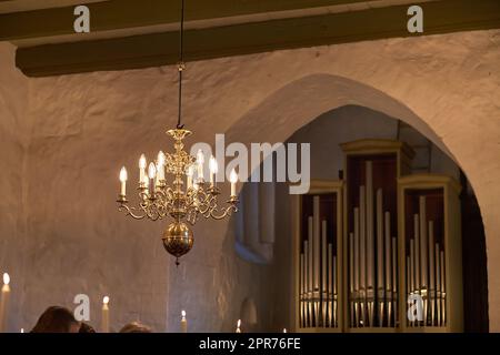 Old fashioned brass chandelier with candle light bulbs hanging from roof or ceiling in a historic building and vintage room. Shiny ornamental, medieval, ancient and antique light fixture in a mansion Stock Photo