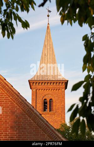 Low angle of a church bell tower against a blue sky. Exterior view of a traditional old religious red brick building on a sunny day. Wall and roof of an historic house or home architecture design Stock Photo