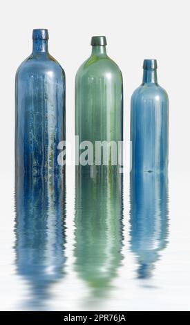 Three glass bottles on white surface with water effect. Old colorful vintage wine bottles arranged against a copy space background with reflections. Side view of unused containers in descending order Stock Photo
