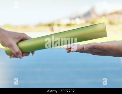 Closeup of two athletes passing a baton during a relay race on a running track. Active fit athlete handing the baton over during a relay race to a team member while running in an sport competition Stock Photo