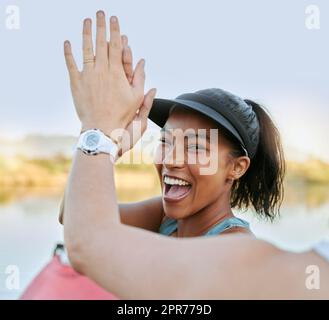 Two friends sharing high five and celebrating their success while being active outdoors. Cheerful woman out kayaking and motivating her partner while enjoying a water activity on a lake in summer Stock Photo