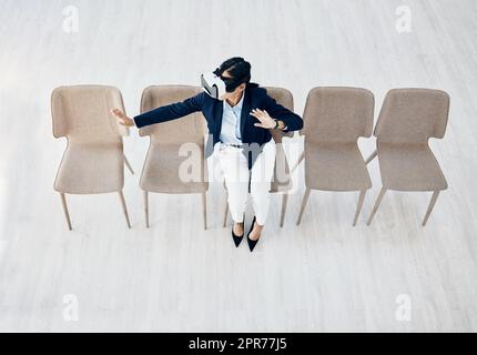 Immersed in a whole new world. High angle shot of a young businesswoman wearing a VR headset while sitting in line in an office. Stock Photo