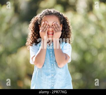 Lets play hide and seek. Shot of an adorable little girl covering her eyes while standing outside. Stock Photo