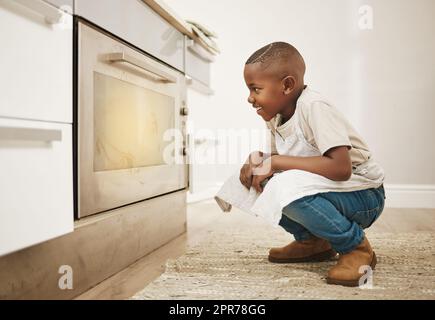 Cant wait to taste these. Shot of a little boy watching his baked goods cook in the oven at home. Stock Photo