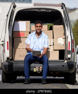 No package goes missing with our tracking system. Portrait of a young delivery man using a digital tablet while loading boxes from a van. Stock Photo