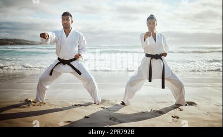 In perfect unison. Full length shot of two young martial artists practicing karate on the beach. Stock Photo