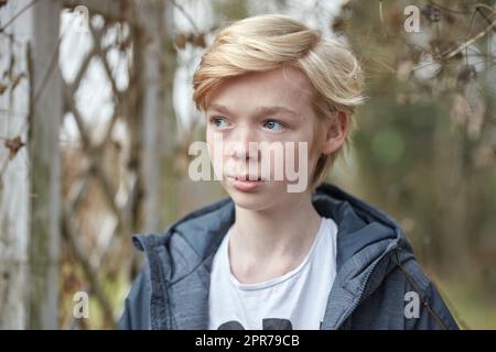 One insecure young teenage boy thinking, feeling shy, nervous alone in city. A preteen or teenager standing outside with social anxiety. Youthful innocent child looking curious, contemplative, unsure Stock Photo