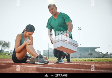 Rushing to the scene for medical attention. a sports paramedic providing first aid to an athlete on a running track. Stock Photo