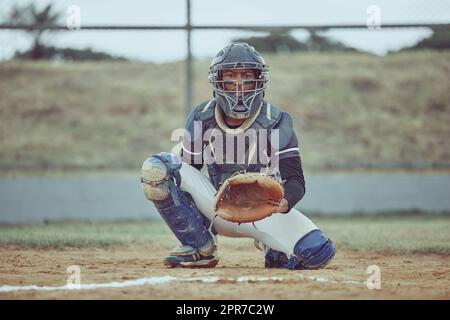 Portrait african american pitcher ready to make a catch with a mitt on a baseball field. Young sportsman in a helmet ready for the ball. Black man athlete playing a game or match on pitch outdoors Stock Photo