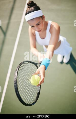 My opponents not going to know what hit them. High angle shot of a young tennis player standing on the court and getting ready to serve during practice. Stock Photo
