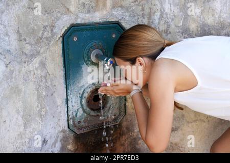 Young woman hydrates herself from a fountain during a heat wave in the city Stock Photo