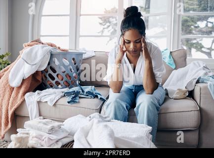 Mothers dont get a break. Shot of an attractive young woman sitting alone in her living room and feeling stressed wile doing the laundry. Stock Photo