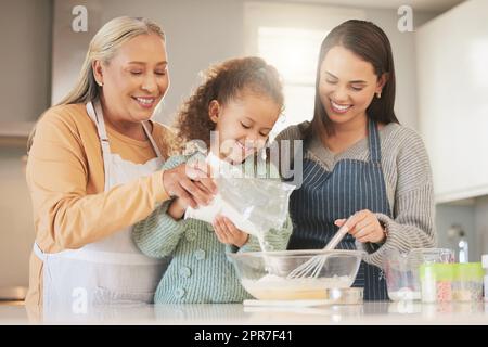 This is a family home, you can smell it. Shot of a little girl baking with her mother and grandmother at home. Stock Photo