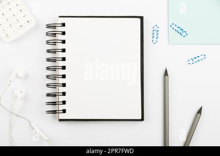 Notebook With Important Message On Desk With Pens, Calculator, Headphones And Paperclips. Notepad With Crutial Information On Table With Pencils And Colored Clips. Stock Photo