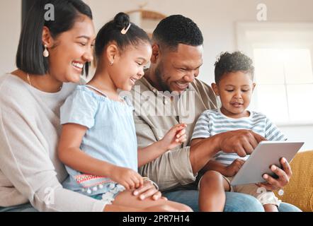 Can you believe how theyve grown. a young family happily bonding while using a digital tablet together on the sofa at home. Stock Photo