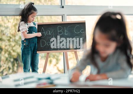 Lets rearrange the alphabet. a young girl writing on a blackboard. Stock Photo