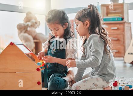 Were building a house for all our dolls to live in. two young girls playing with a dollhouse. Stock Photo