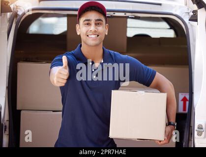 I promise the speediest delivery to you. Portrait of a young delivery man showing thumbs up while loading boxes from a van. Stock Photo