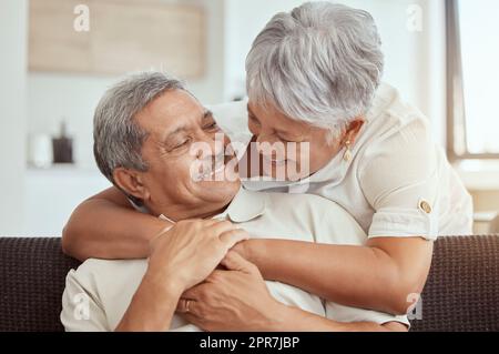Mixed race senior couple hugging in a living room at home. Smiling elderly husband and wife holding each other and embracing in lounge. Happy playful retired man and woman bonding and feeling in love Stock Photo