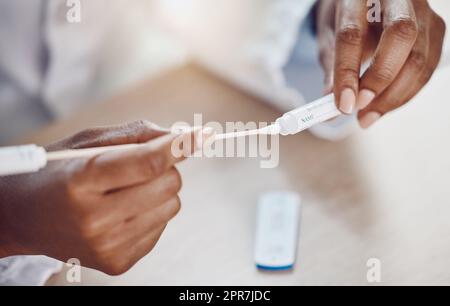 Above closeup african american woman doctor using a sterile swab stick while sitting at her desk in the hospital. Testing for the corona virus pandemic. Stop the spread of covid 19 and get tested Stock Photo