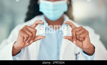 Doctor holding bottles of the covid antidote. African American doctor holding vials of the corona virus cure. Saving the world one bottle at a time. Healthcare worker holding bottles of medicine Stock Photo