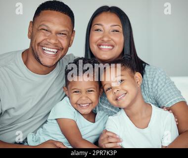 Portrait of a happy young mixed race family with two children wearing pyjamas and sitting at home together. Loving little sister and brother spending time with their parents on the weekend Stock Photo