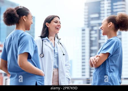Young caucasian doctor in a lab coat standing outside and talking to mixed race nurses in scrubs. Diverse group of healthcare professionals. African American medical nurses in uniform with a physician Stock Photo