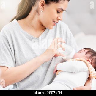 Young hispanic mother feeding her newborn baby a milk bottle and bonding with her. Little baby asleep in her mothers arms in her bedroom. Small, tiny baby drinking milk and falling asleep Stock Photo
