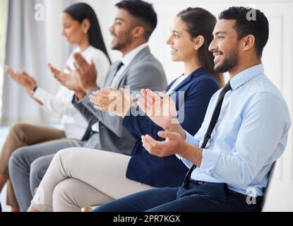 Group of diverse businesspeople clapping and celebrating success during interview. Team of applicants together, attending office seminar. Candidates in line for job opening, vacancy and opportunity Stock Photo