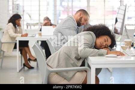 Two young mixed race call center agents sleeping at their desks while working in an office at work. Hispanic customer service workers taking a nap while working together Stock Photo