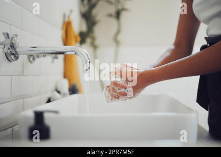 Close up of female hands using soap and washing hands under faucet with clean water. Woman rubbing hands together before rinsing for coronavirus prevention Stock Photo