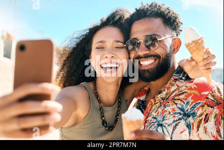 Making summer memories. an affectionate young couple taking selfies while enjoying ice creams on the beach. Stock Photo