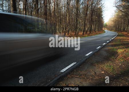 A car driving fast on a road through the forest Stock Photo